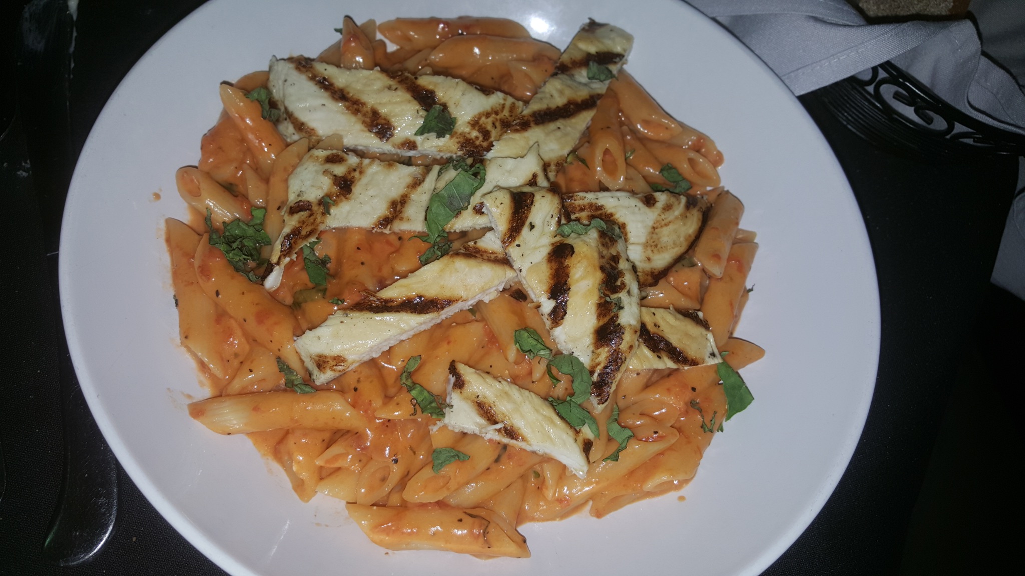 Penne pasta in a creamy tomato sauce topped with grilled chicken and basil